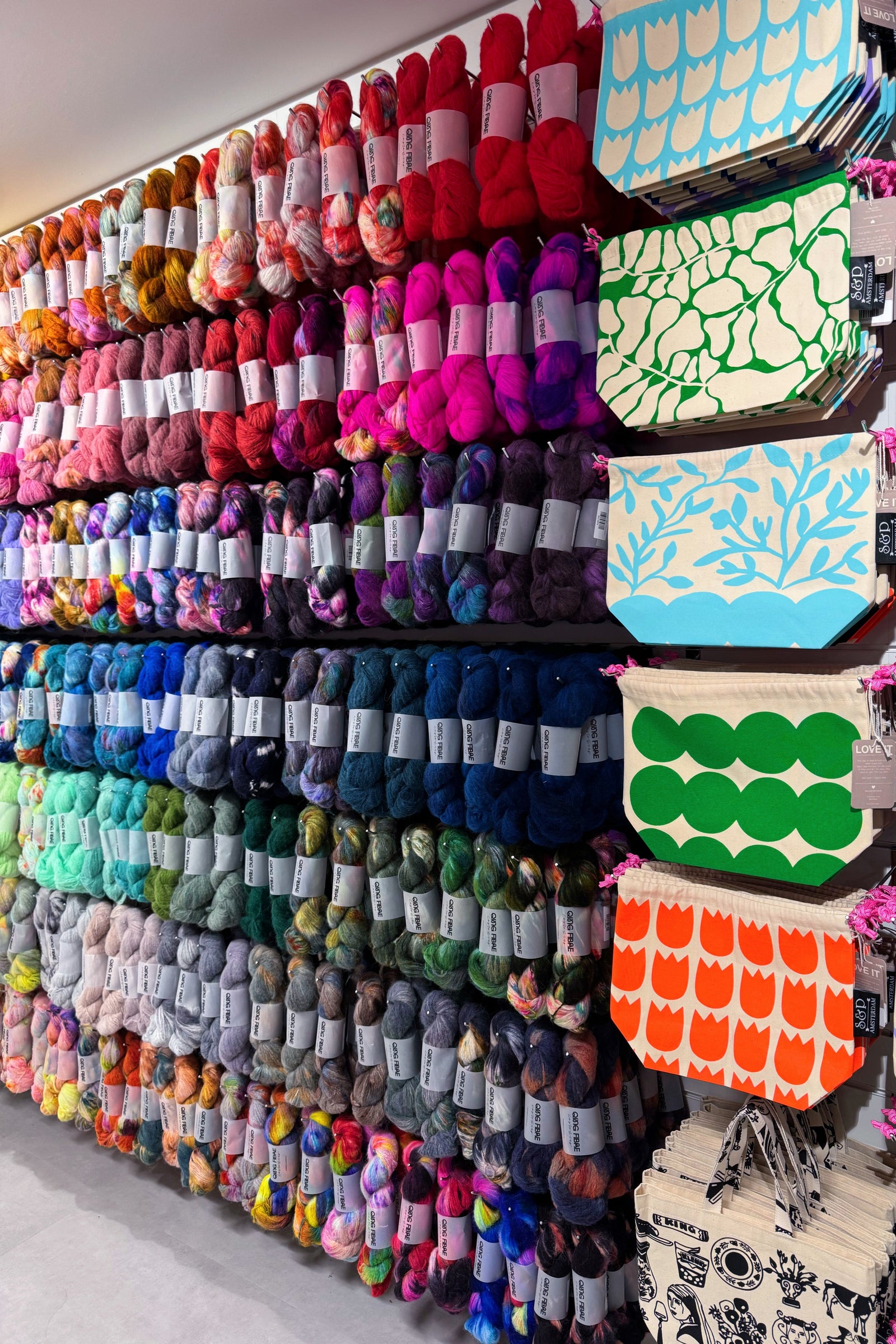 Wall of colorful yarn and patterned project bags in a store setting