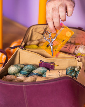 This image shows Project 39 - Aubergine, filled with yarn and notions. The bag is part of a collaboration between Re:Designed and Westknits. Stephen West is holding a notions from the bag.