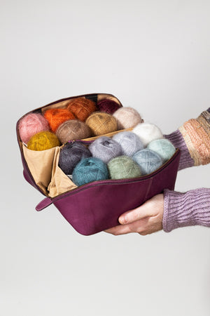 This image shows Project 9 - Aubergine, filled with yarn. The bag is part of a collaboration between Re:Designed and Westknits. Stephen West is holding the bag in his hands.