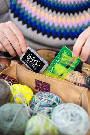 This image shows Project 10 - Aubergine, filled with yarn and needles. The bag is part of a collaboration between Re:Designed and Westknits. Stephen West is holding a notions from the bag.