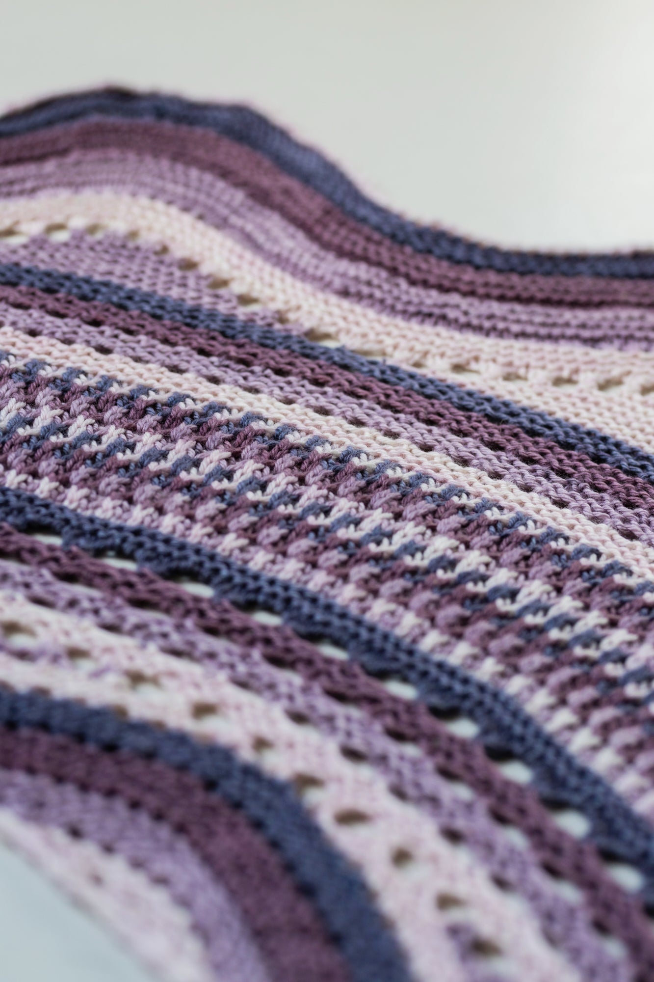 This image shows a close-up of the Eyelet Journey Shawl by Westknits. The sample is knitted in purple and pink gradients.