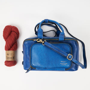 This image shows a denim project bag from the Westknits x Re:Designed collaboration next to a skein of West Wool Tandem in red.