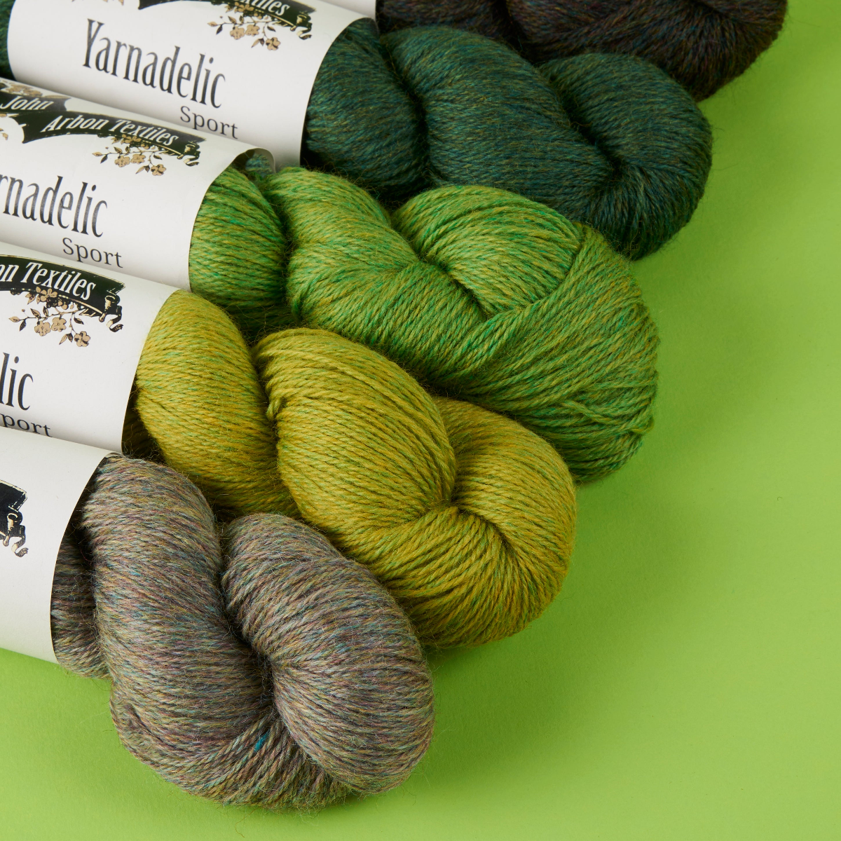 Yarnadelic Sport yarn skeins in various green shades on a green background