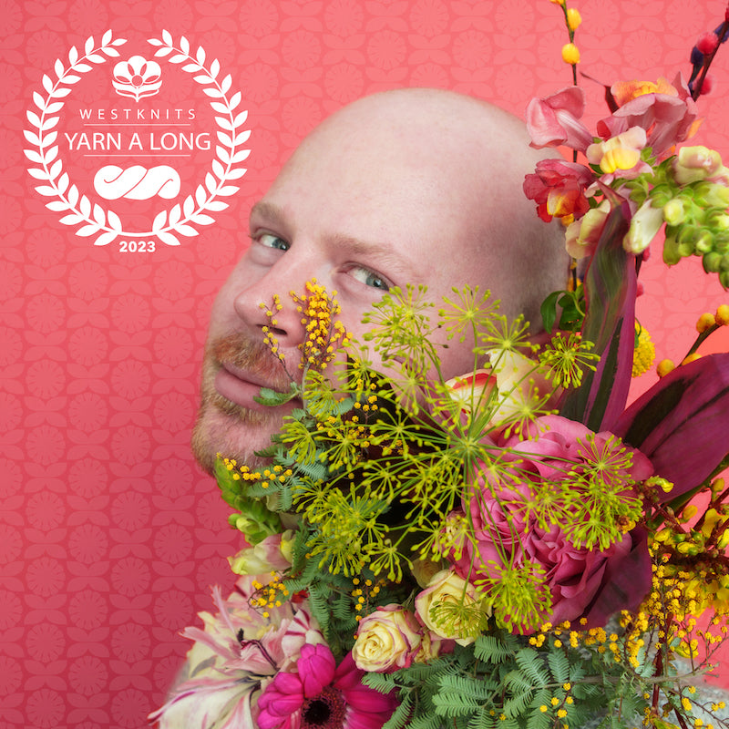 Photo of Stephen holding a bouquet of pink and purple flowers. He is staring in the camera with a playful smile. He is against a pink background decorated with flowers. A white Westknits YAL logo is on the top left corner.