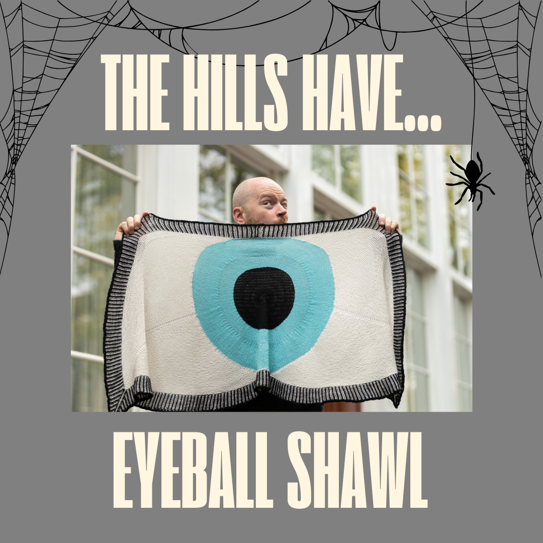 Stephen West holding up a shawl with a pattern that resembles a blue eyeball.  Text reads The Hills have Eyeball Shawl.