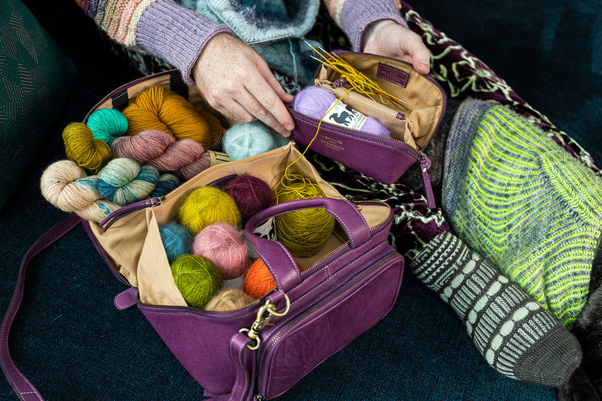 This image shows Project 39 and 41 - Aubergine, filled with yarn and needles. The bag is part of a collaboration between Re:Designed and Westknits. Stephen West is holding one of the bags.