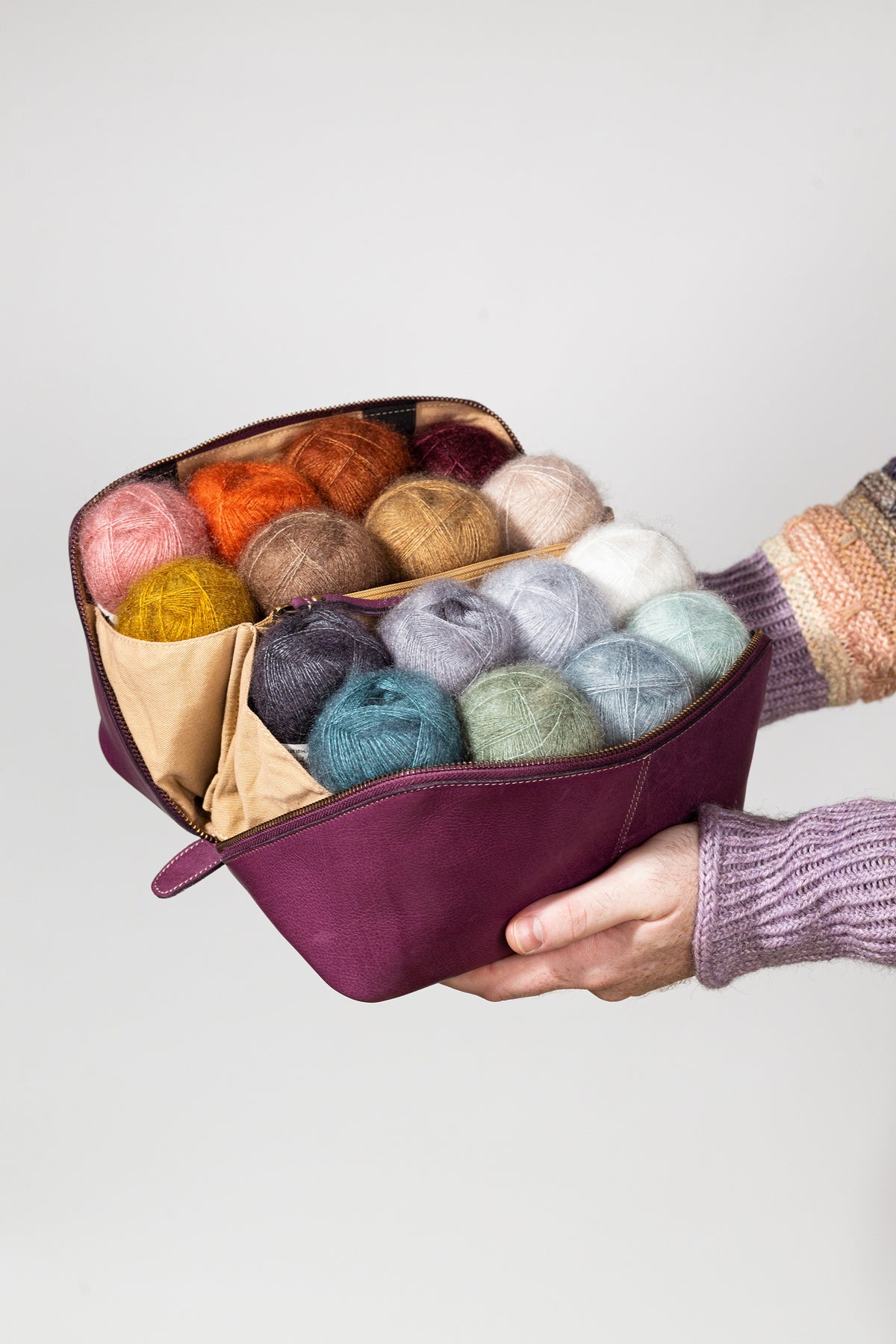 This image shows Project 9 - Aubergine, filled with yarn. The bag is part of a collaboration between Re:Designed and Westknits. Stephen West is holding the bag in his hands. 
