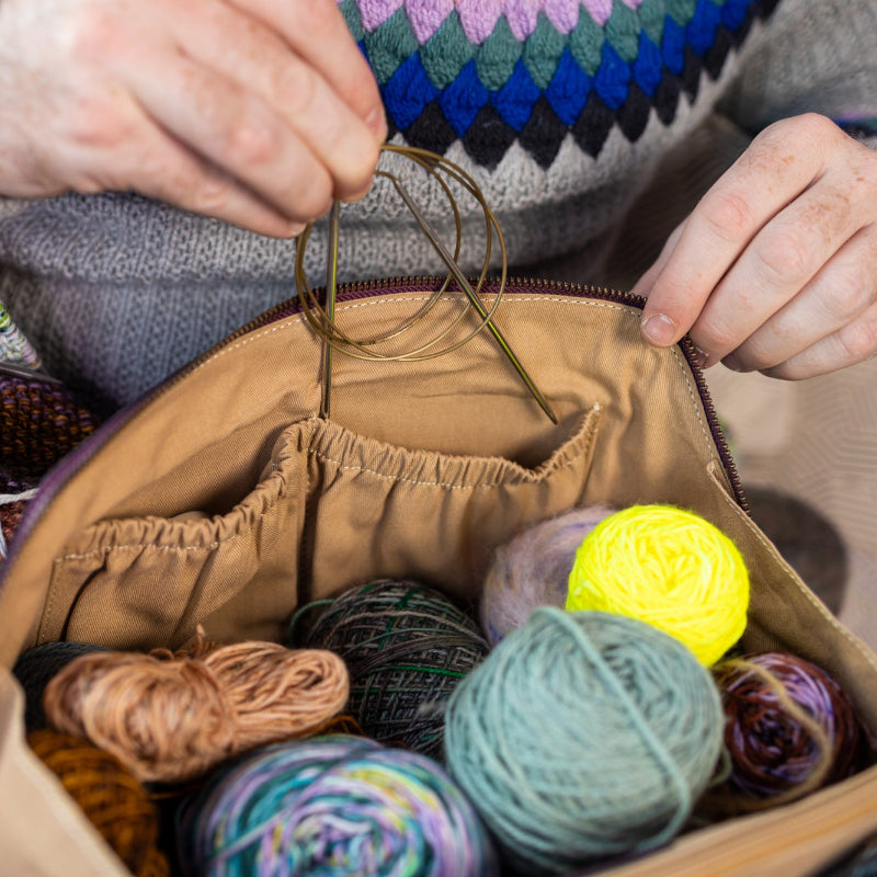 This image shows Project 10 - Aubergine, filled with yarn and needles. The bag is part of a collaboration between Re:Designed and Westknits. Stephen West is holding a needle from the bag.