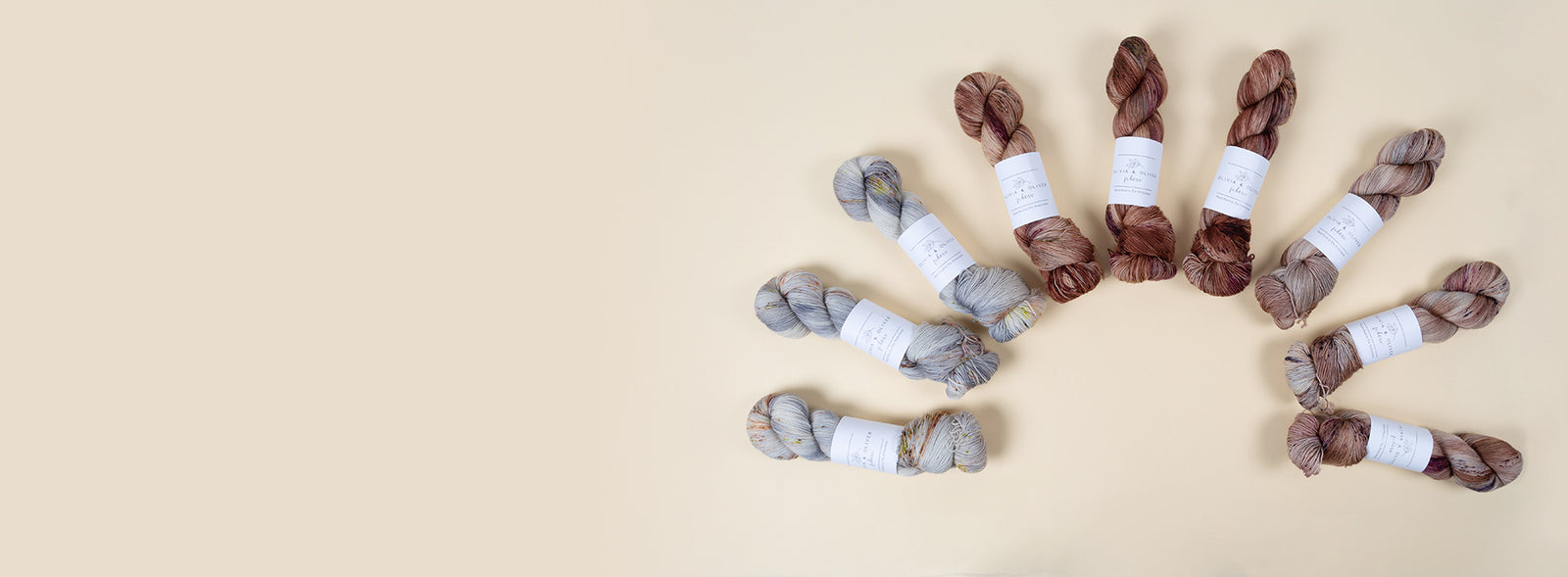 This image shows some skeins of Olivia & Oliver yarn in brown and cream tones, laid in a semicircle, on a beige background. 