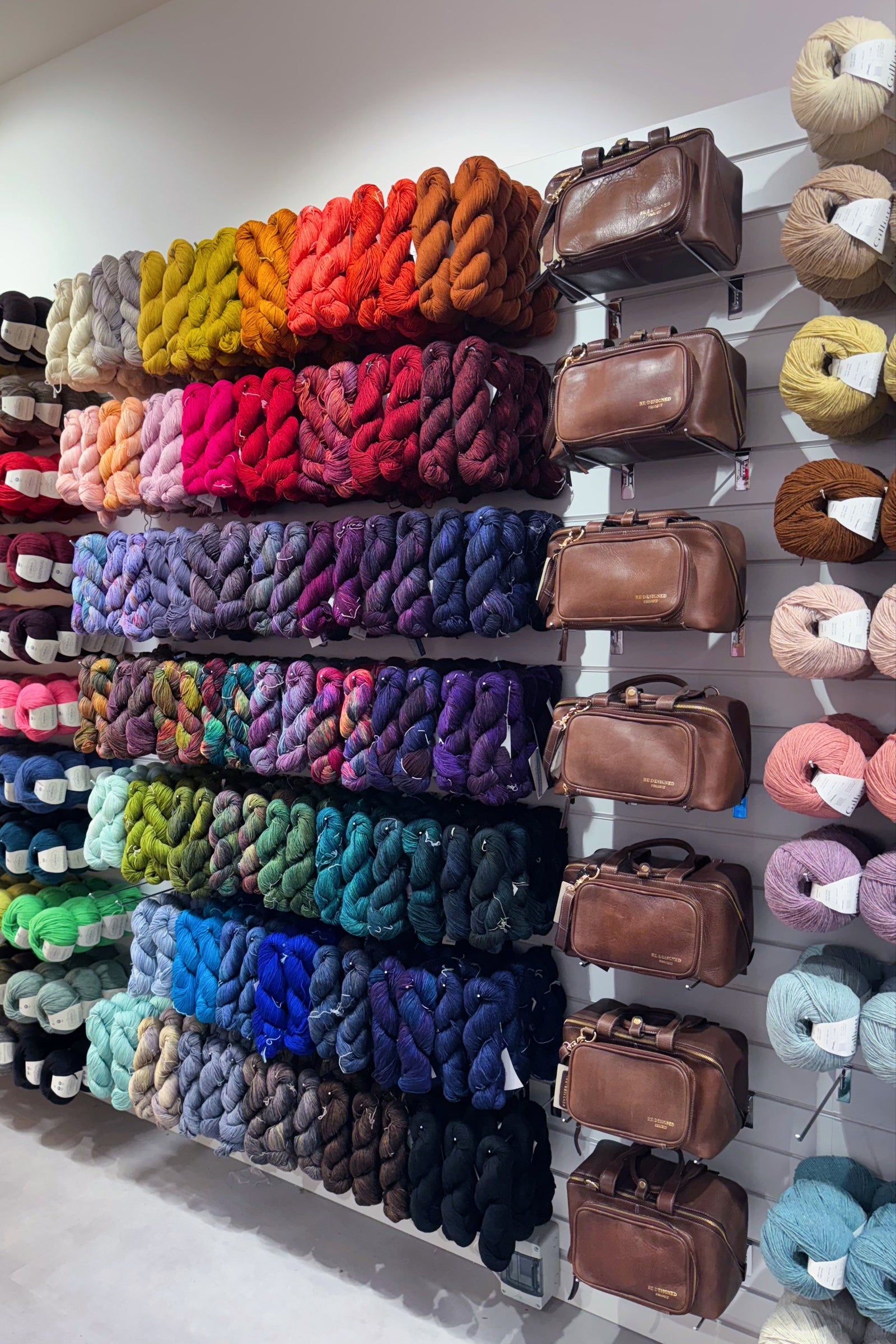 Wall display of colourful yarn and brown leather project bag bags.