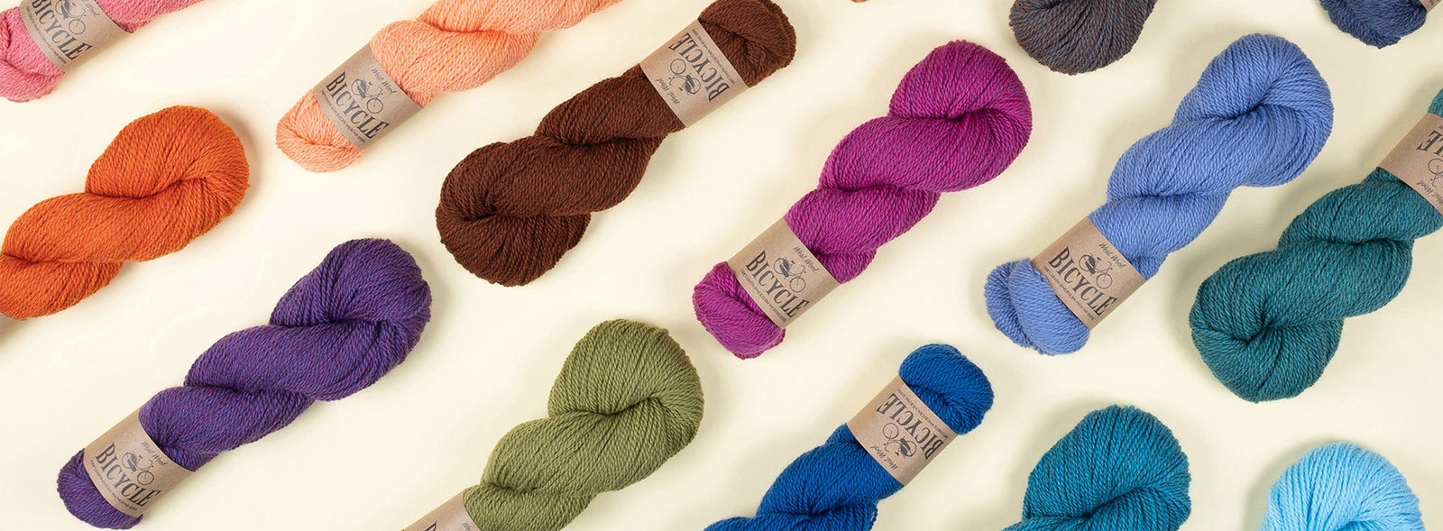 This image shows the variety of new colours of Bicycle from West Wool on a pastel yellow background. The colours include brown, coral, orange, blue and green. 