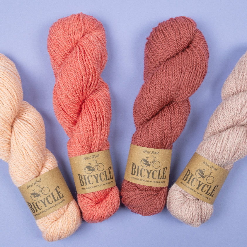 Assorted skeins of West Wool yarn in pink shades on a purple background