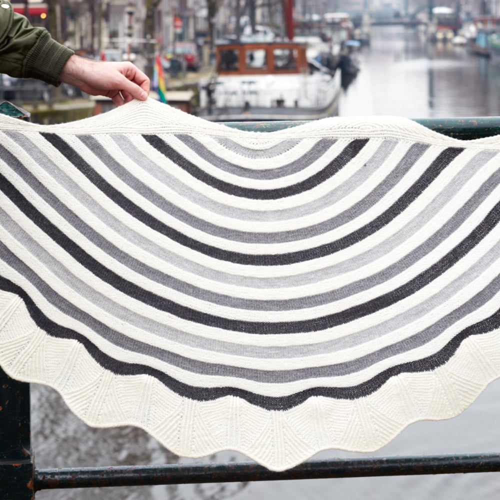 This image shows a beautifully knitted sample of the Canal Ring Shawl from Westknits in contrasting grey and white tones. 