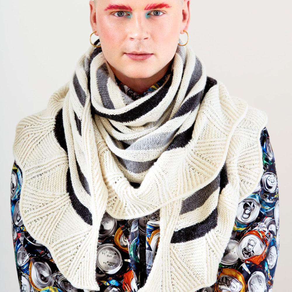 This image shows Stephen West wearing a beautifully knitted sample of the Canal Ring Shawl from Westknits in contrasting grey and white tones. 