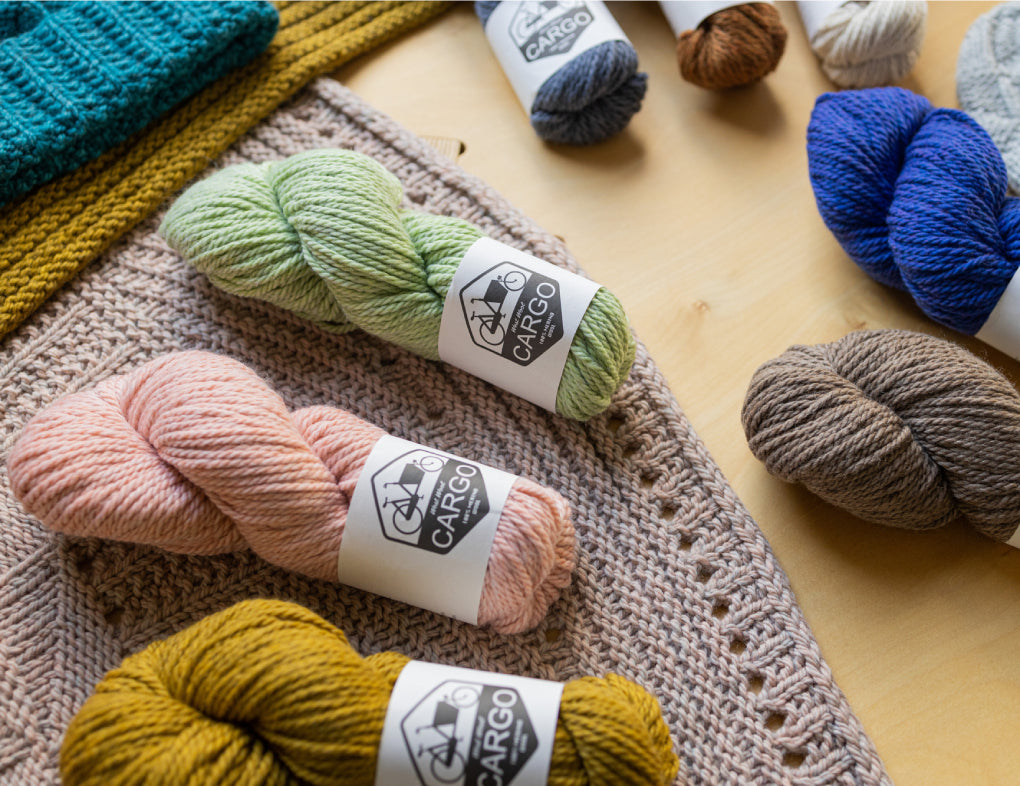 This image shows various skeins of chunky weight Cargo  from West Wool  in various colours, laid on various knitted samples. 
