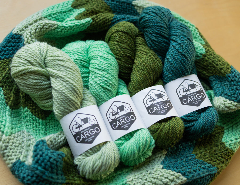 This image shows four skeins of West Wool Cargo in green gradient, laid on a beautifully knitted cowl in the same colours. 