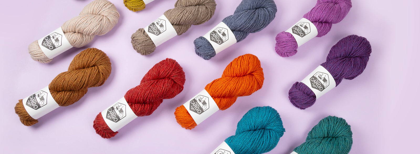 This image shows various skeins of West Wool Cargo in various colours, on a lilac background. 