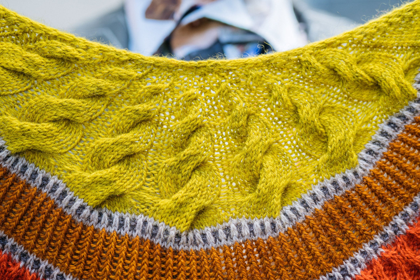 This image shows a beautifully knitted sample of the Corrie Shawl Sample by Westknits in orange, yellow and brown tones. 