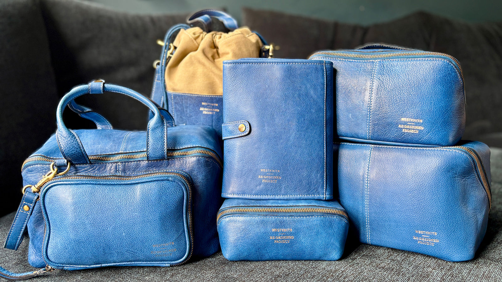 This image shows the entire collection of denim project bags from the Westknits x Re:designed collaboration. The 6 bags are laid on a sofa. 