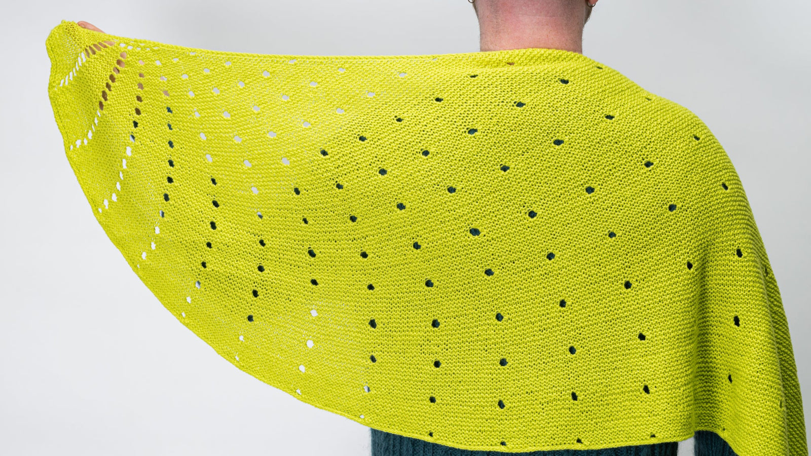 Person wearing a bright green knitted shawl with a dotted pattern on a plain background