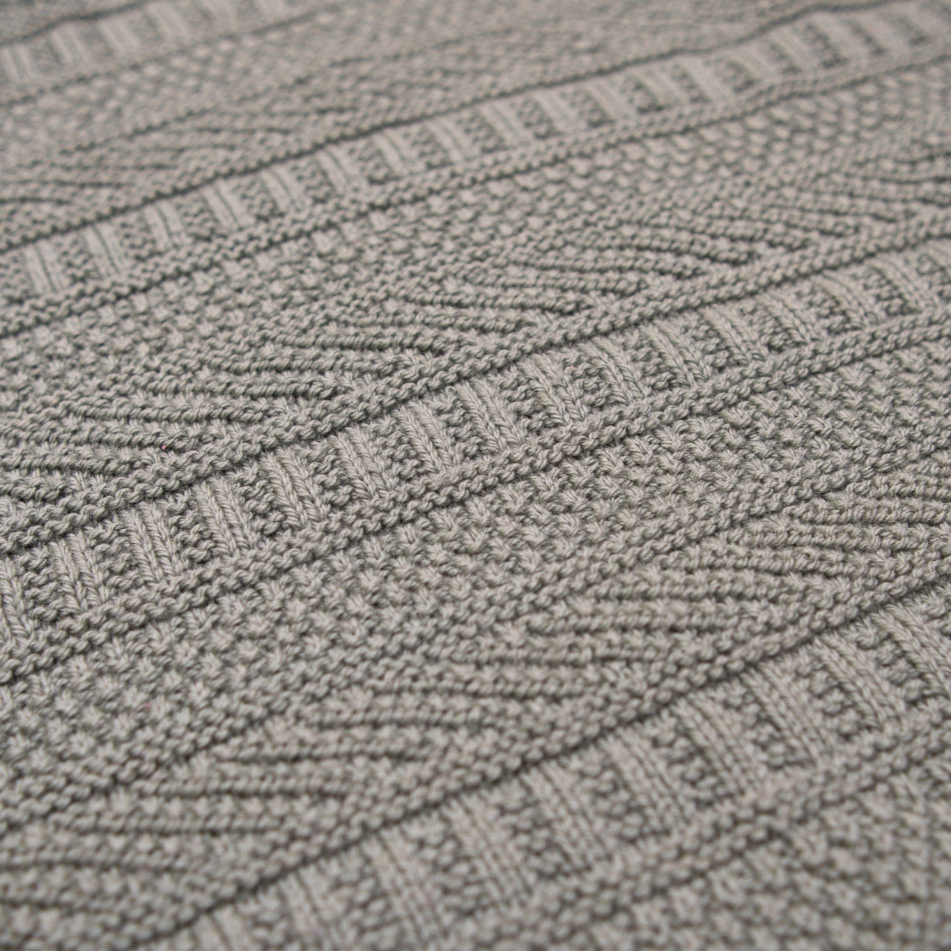 This image shows a detail of a knitted sample of the Dustland Blanket by Westknits in dusty green yarn. 