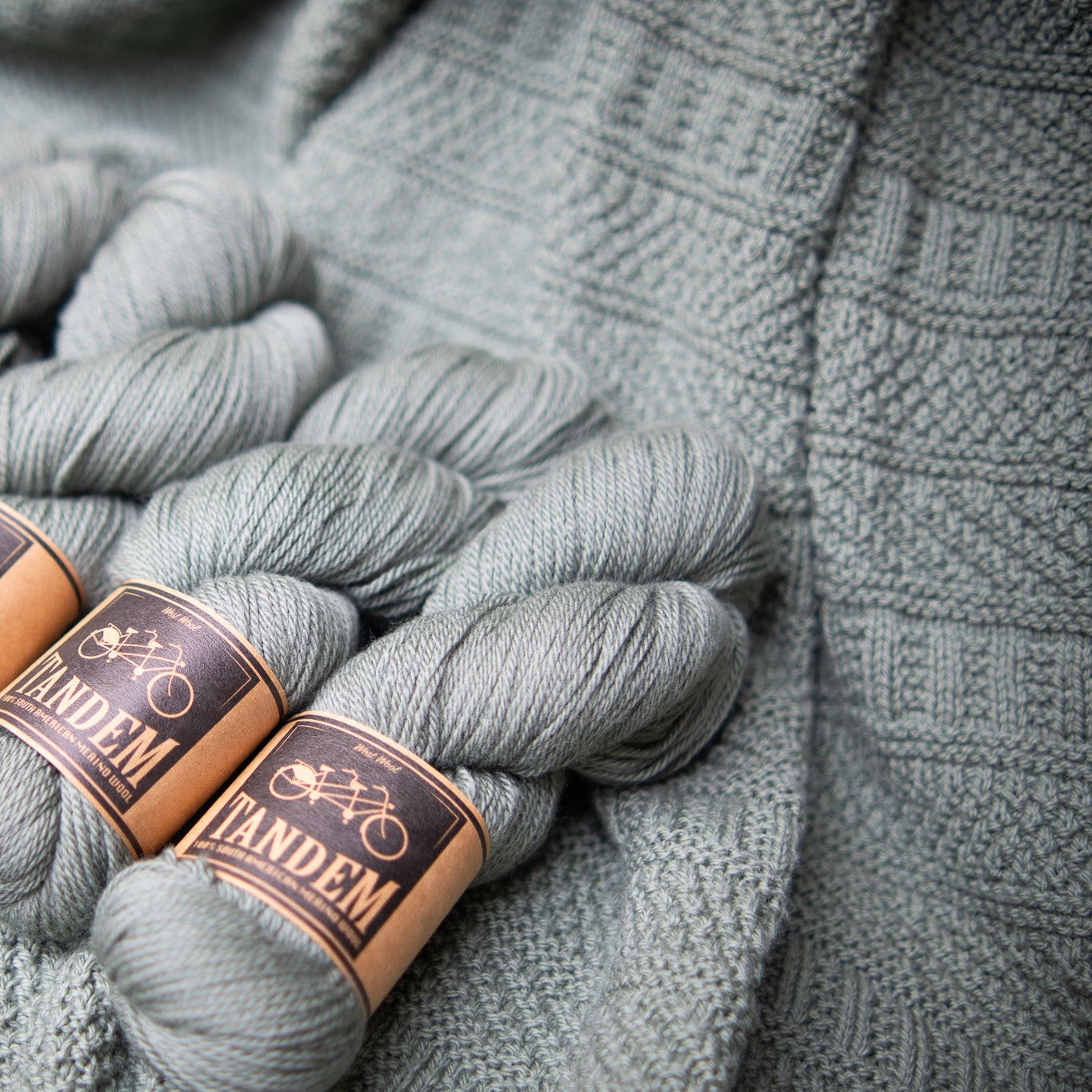 This image shows a detail of a knitted sample of the Dustland Blanket by Westknits in dusty green yarn. 