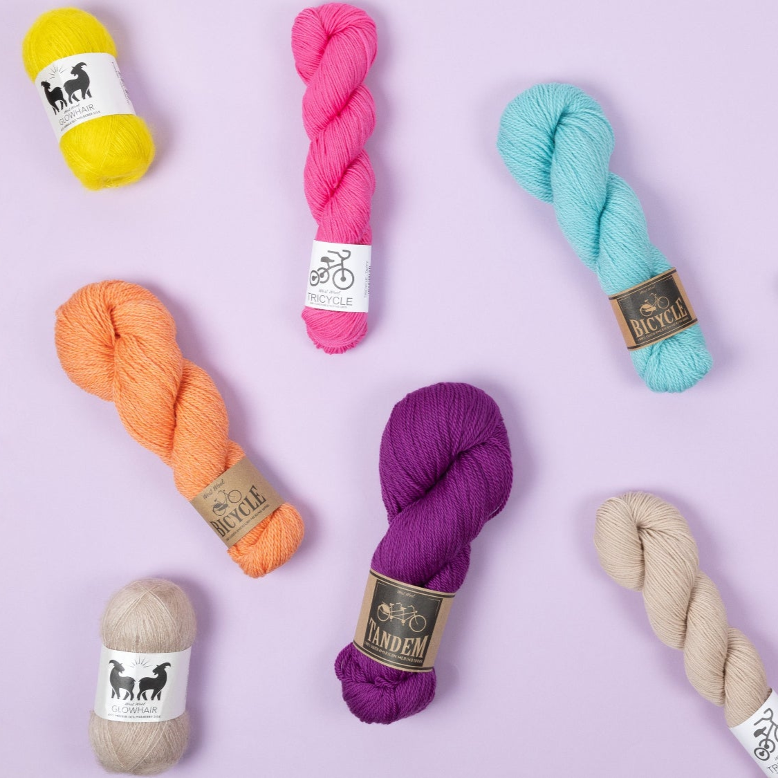 Various skeins of West Wool yarn in bright colours on a lilac background 