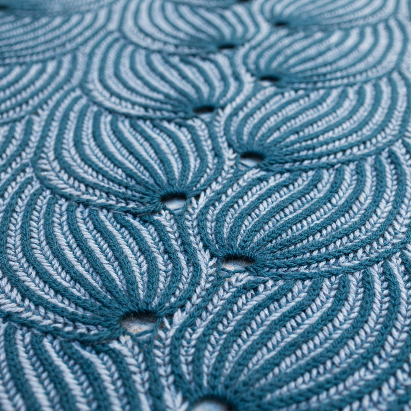 This image shows a detail of a beautifully knitted sample of the Flying Foxtail Blanket by Westknits in grey and blue tones. 