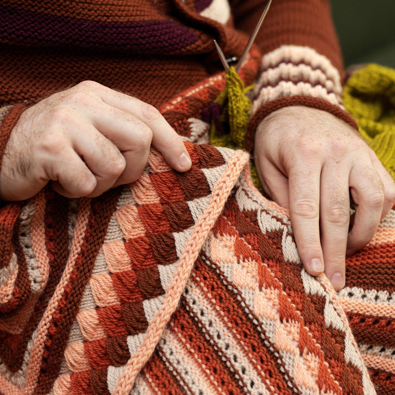 This image shows a detail of a beautifully knitted sample of the Geogradient Blanket by Westknits in warm pink and red tones.