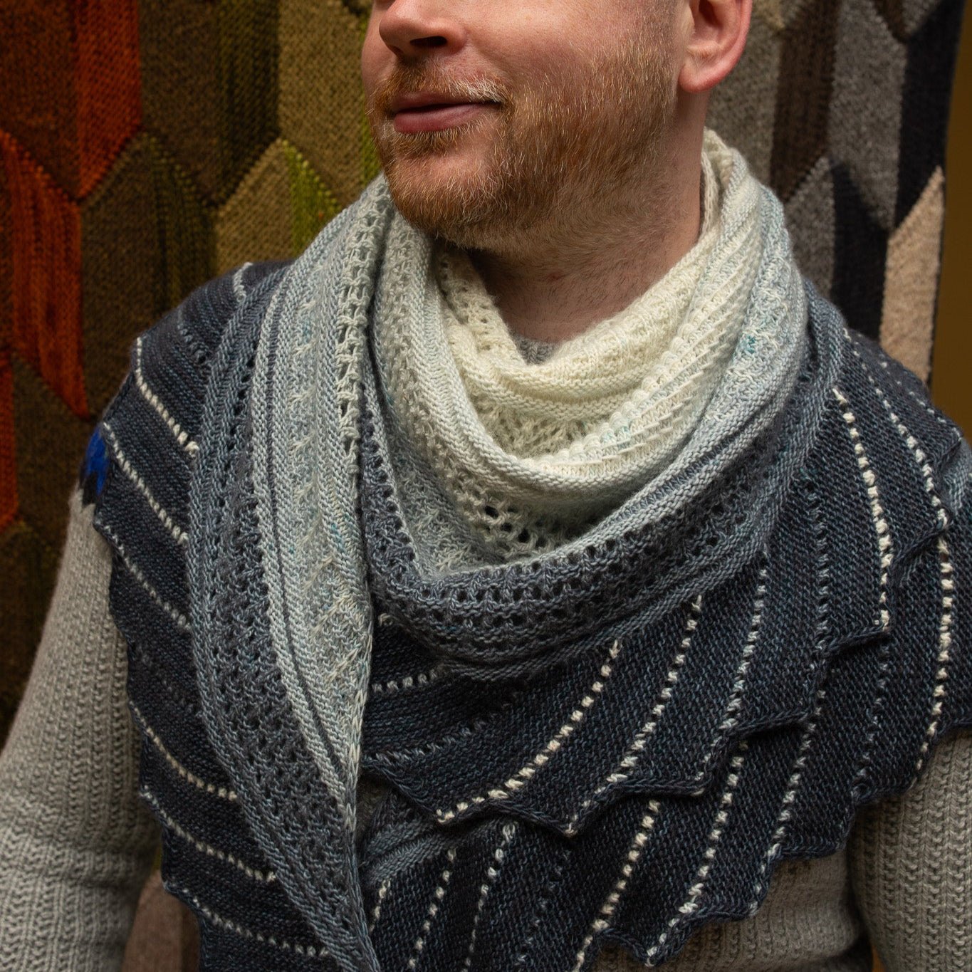 This image shows Stephen West wearing a sample of the Glittering Snowscape Shawl by Westknits in cool tones. 