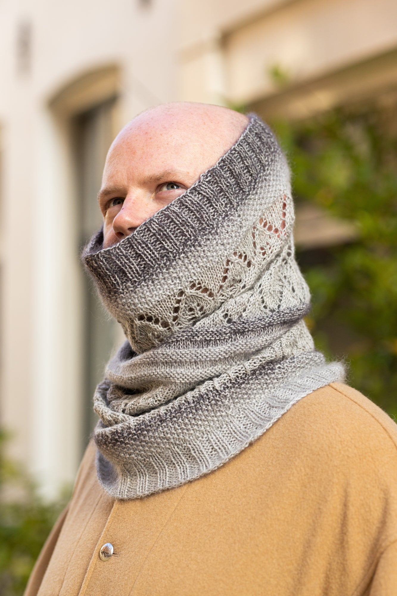 Stephen West wearing a grey sample of the Glowhair Frost Cowl by Westknits. The background shows a street in Amsterdam. 