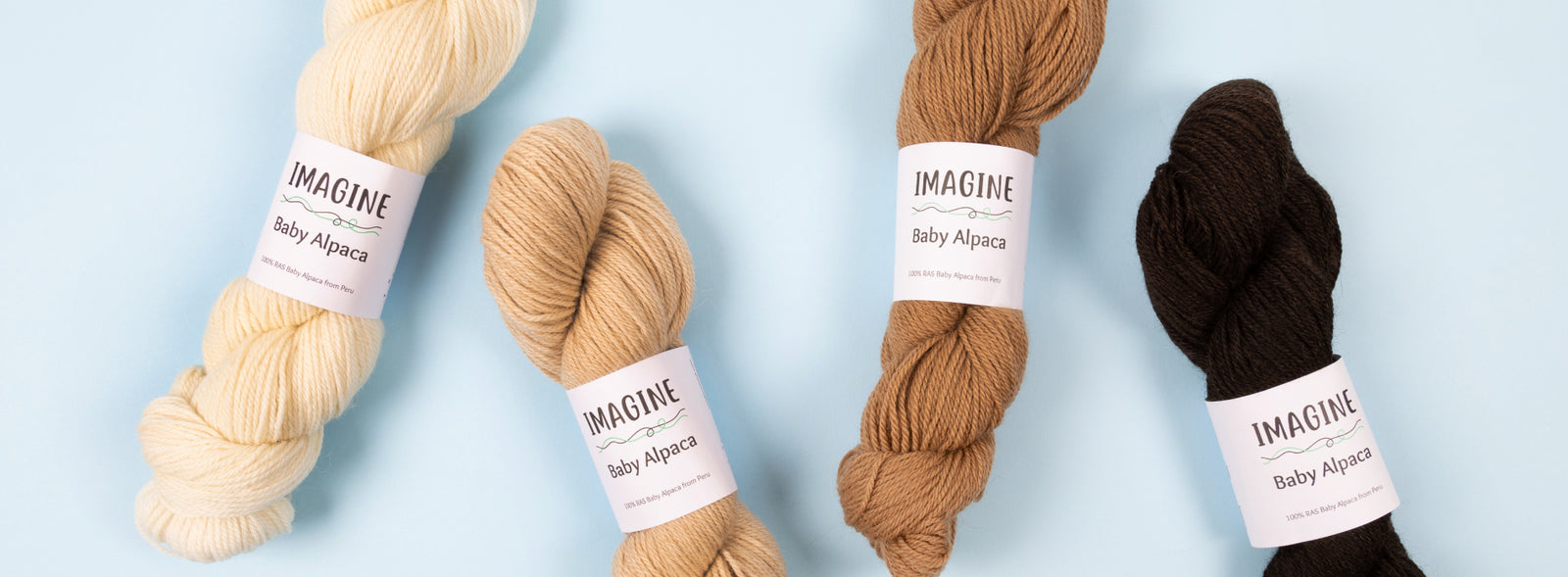 This image shows 4 skeins of Baby Alpaca yarn from Imagine in brown and cream tones, on a light blue background. 