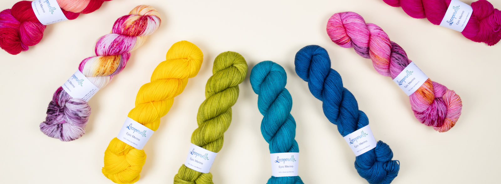 This image shows various skeins of Epic Merino from Locoporella in a rainbow on a pastel yellow background. 