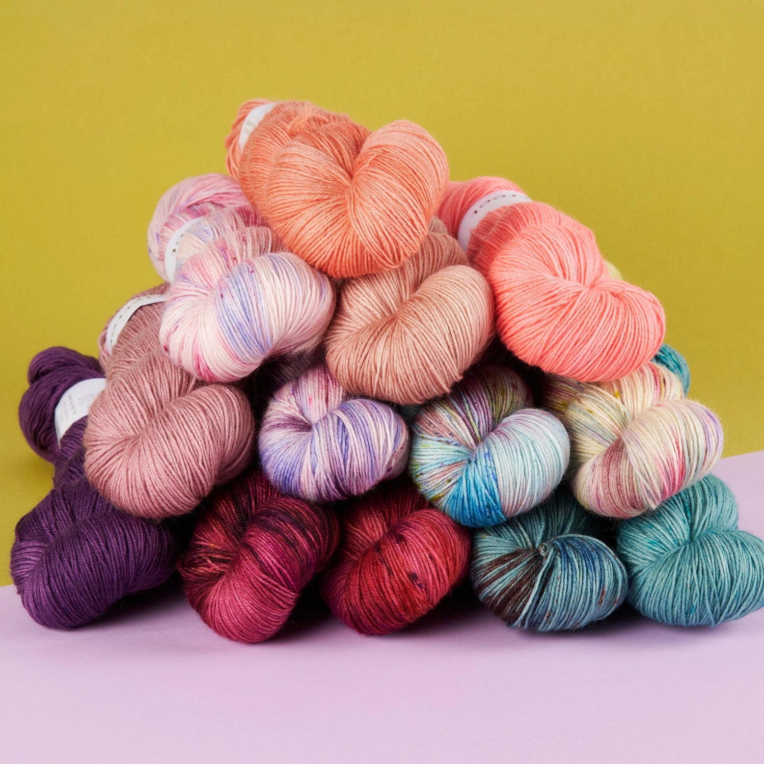 Colorful skeins of yarn on a pink and green gradient background