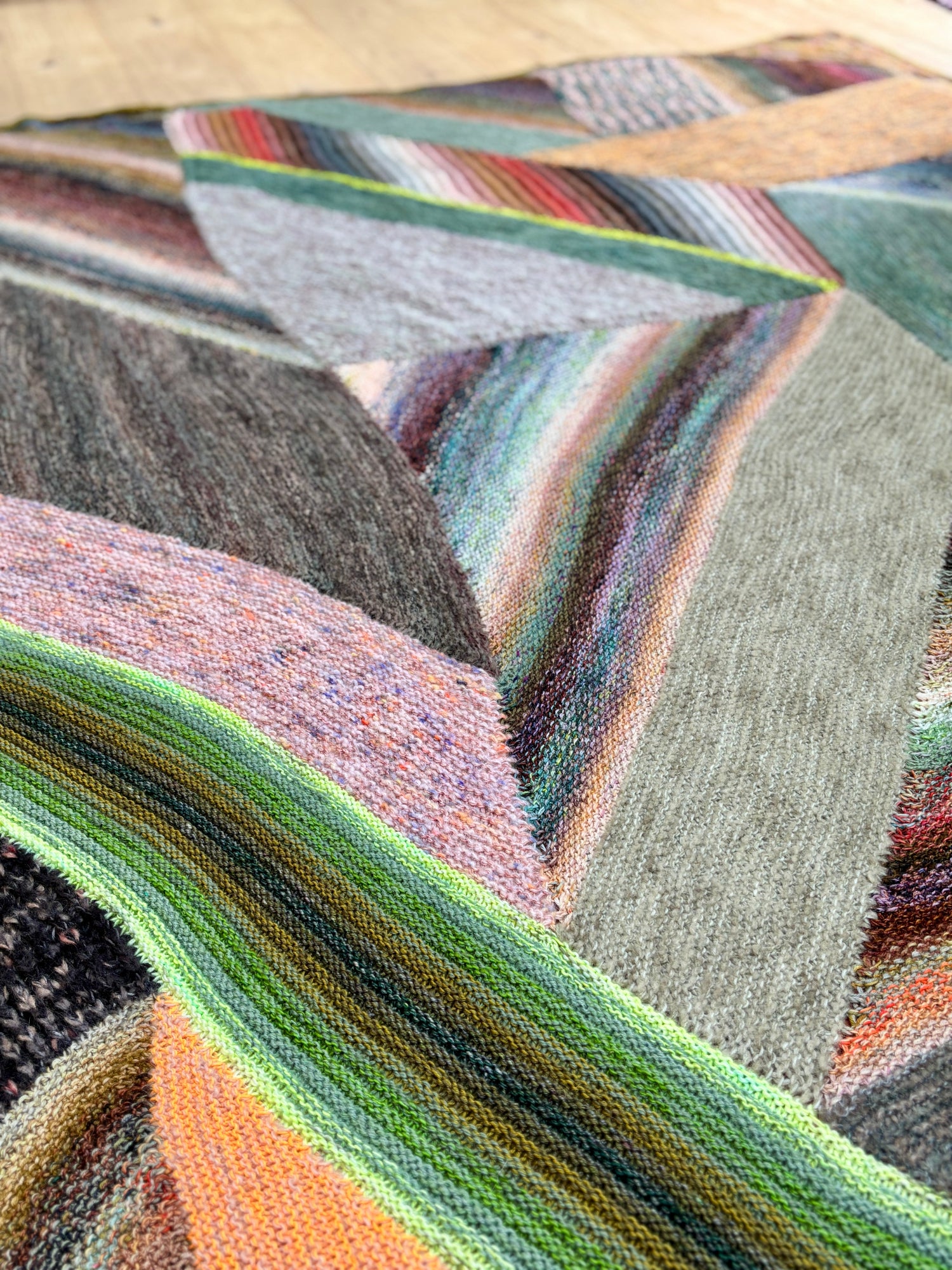 This image shows a detail of a sample of the beautifully knitted Marled Magic Blanket from Westknits. The blanket is knitted with various colours and has a patchwork layout. 