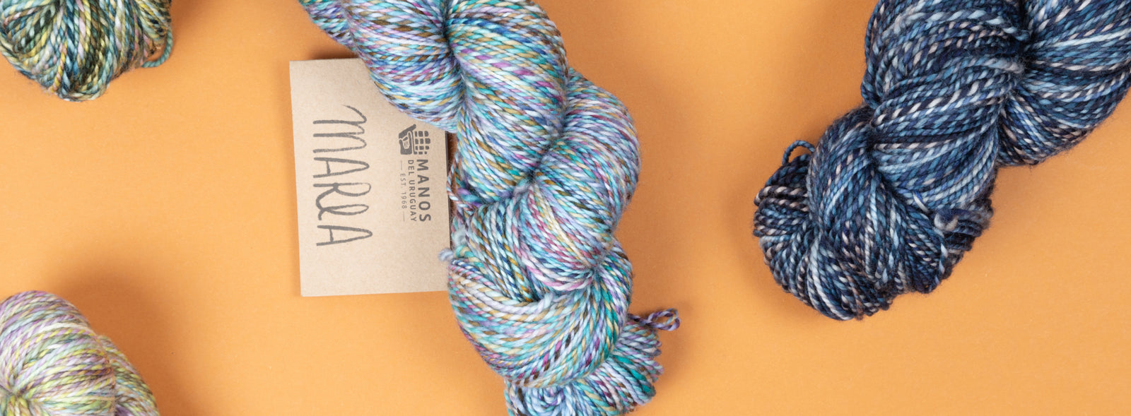 This image shows various skeins of Marla from Manos del Uruguay on an orange backround. 