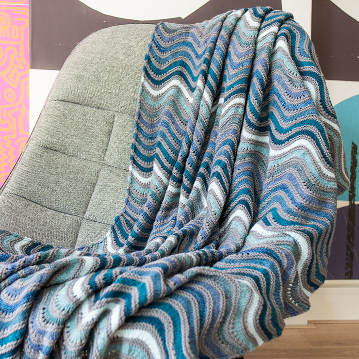 This image shows a beautifully knitted sample of the Painting Waves Blanket in cool blue and grey tones. 