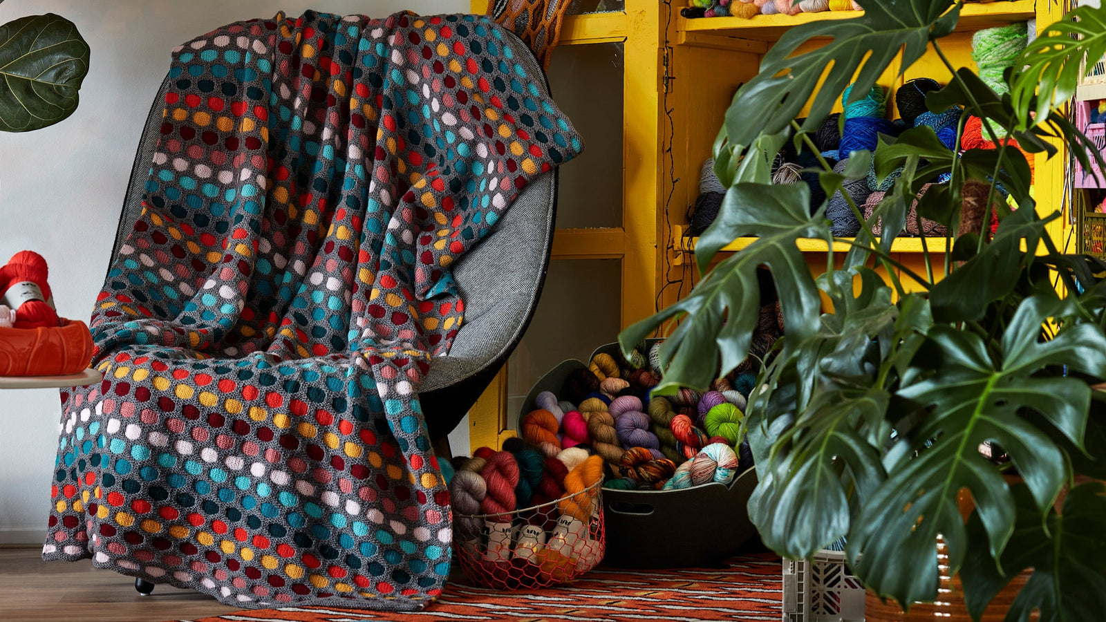 This image shows a knitted sample of the Painting Honeycombs Blanket by Westknits in various colours, including grey, yellow, orange, blue. 