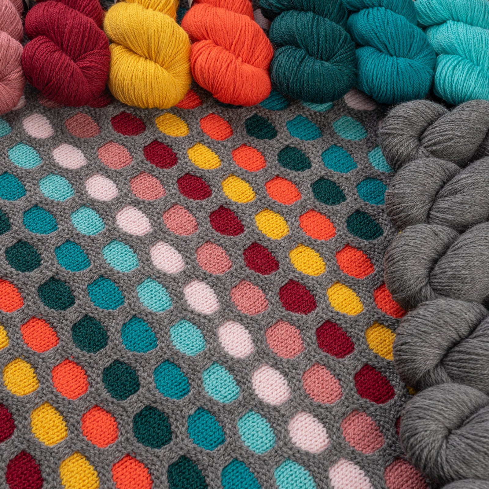 This image shows a detail of the knitted sample of the Painting Honeycombs Blanket by Westknits in various colours, including grey, yellow, orange, blue. 