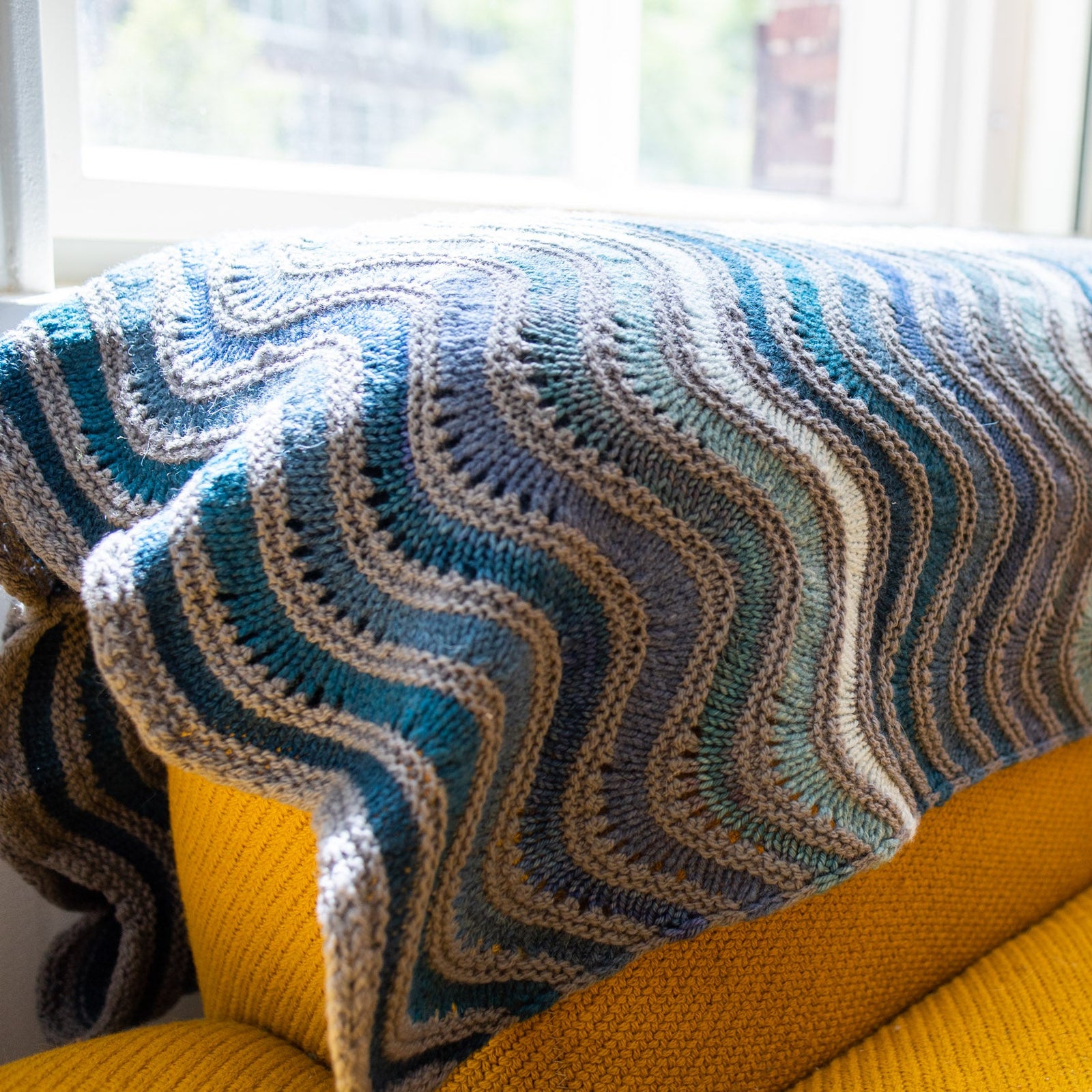 This image shows a detail of a beautifully knitted sample of the Painting Waves Blanket in cool blue and grey tones. 