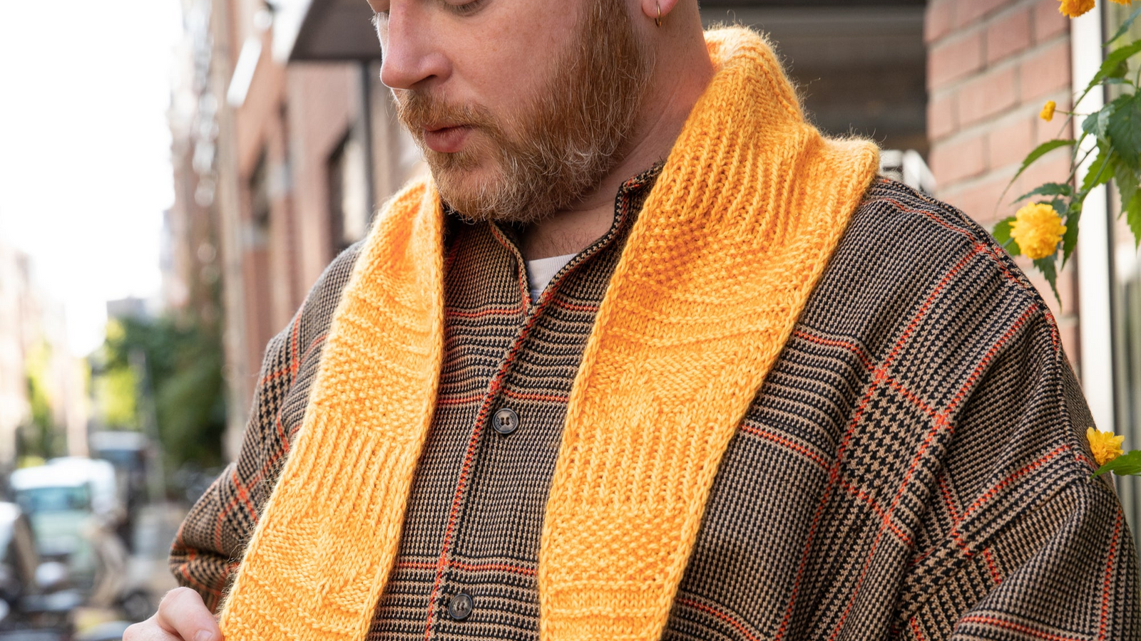 Stephen West wearing a hand knitted sample of an orange skinny scarf. 