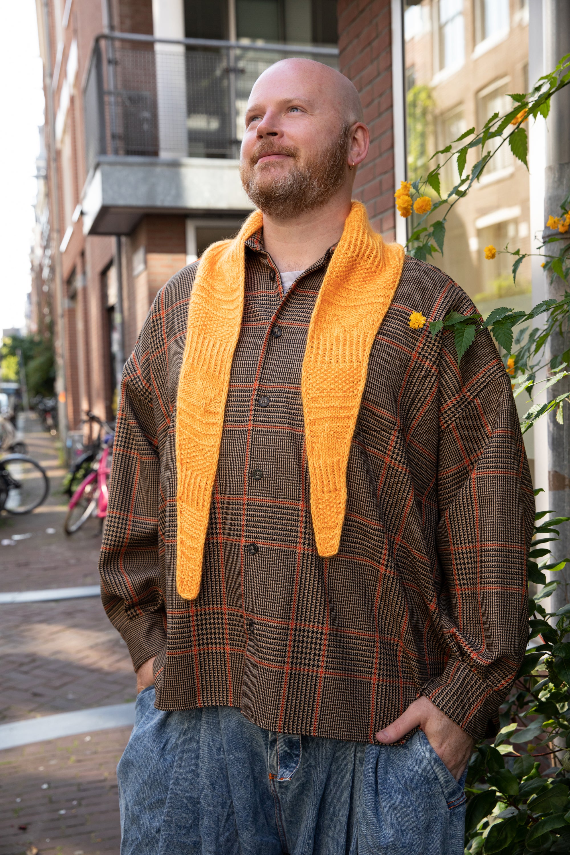 Stephen West wearing a hand knitted sample of an orange skinny scarf. 