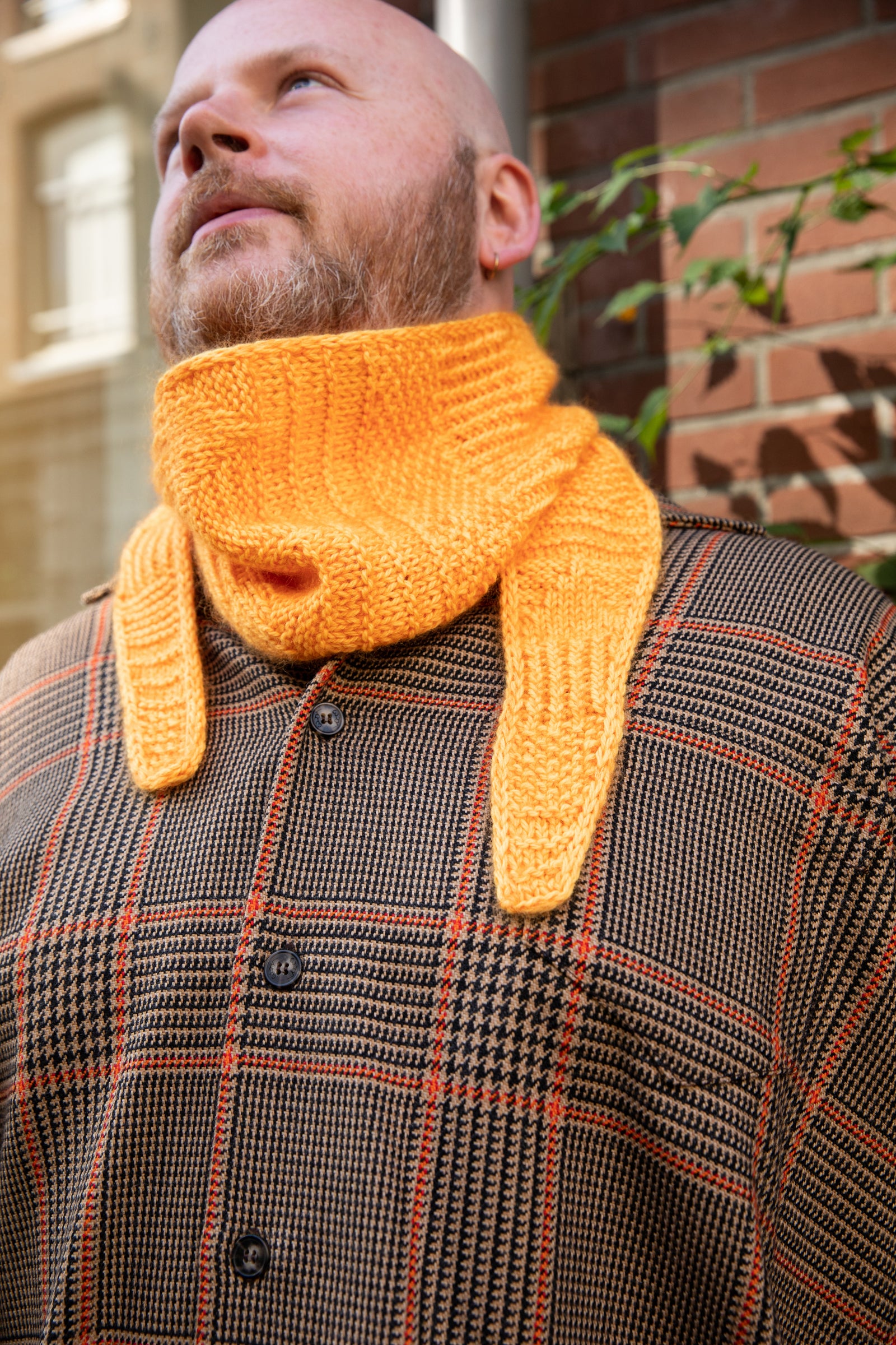 Stephen West wearing a hand knitted sample of an orange skinny scarf. 