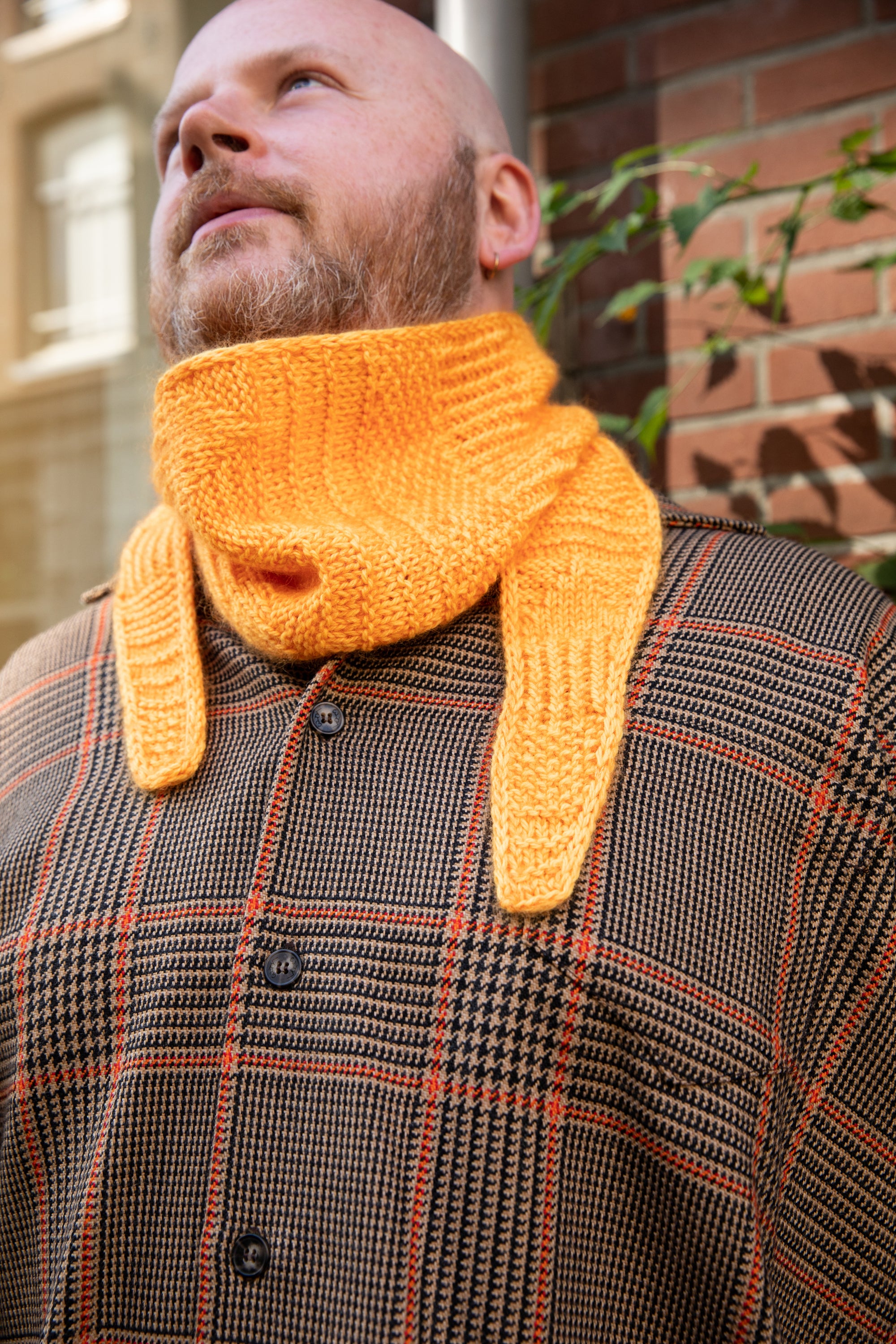 Stephen West wearing a hand knitted sample of an orange skinny scarf. 