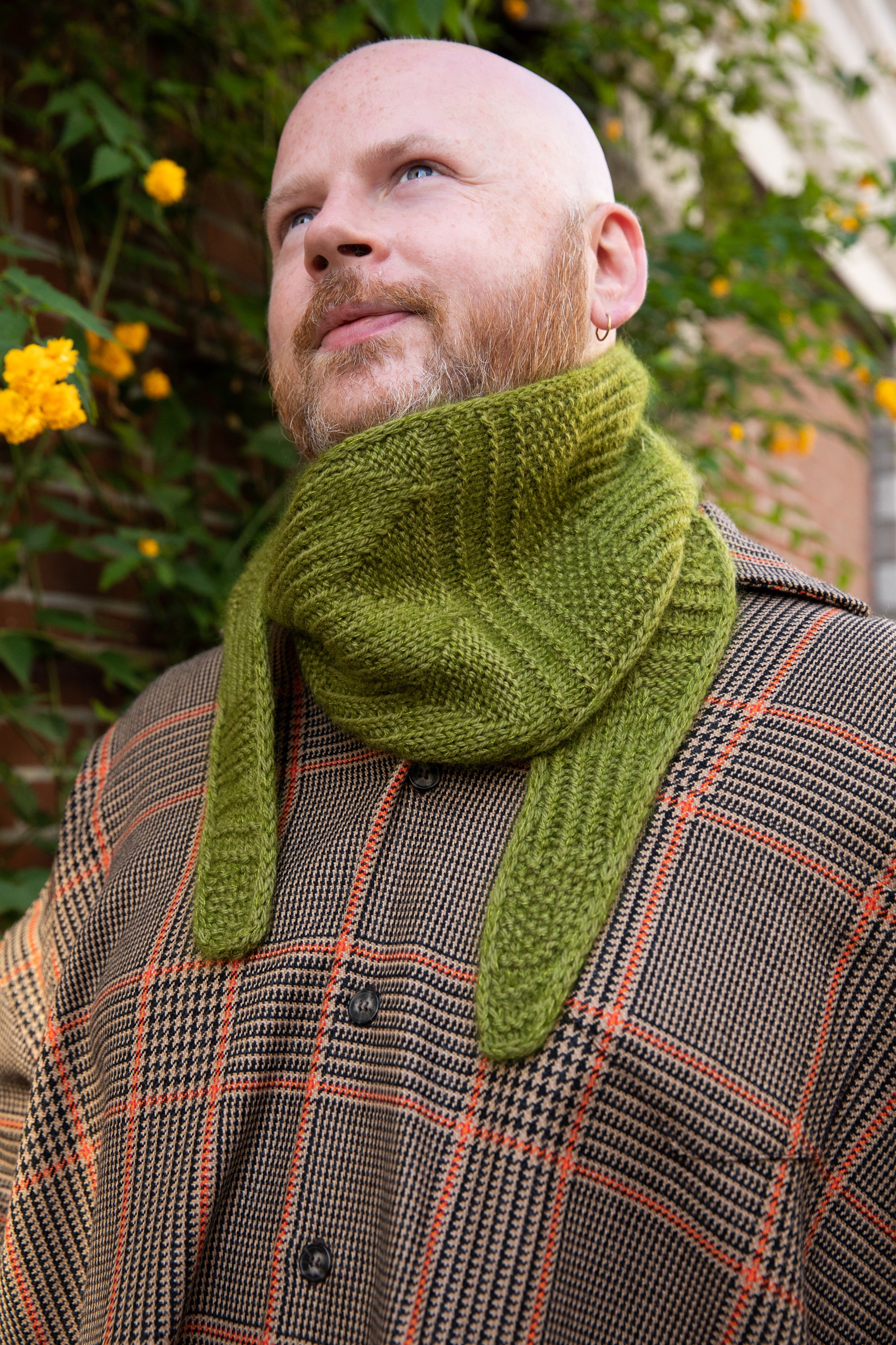 Stephen West wearing a hand knitted sample of a green skinny scarf. 