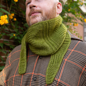Stephen West wearing a hand knitted sample of a green skinny scarf. 