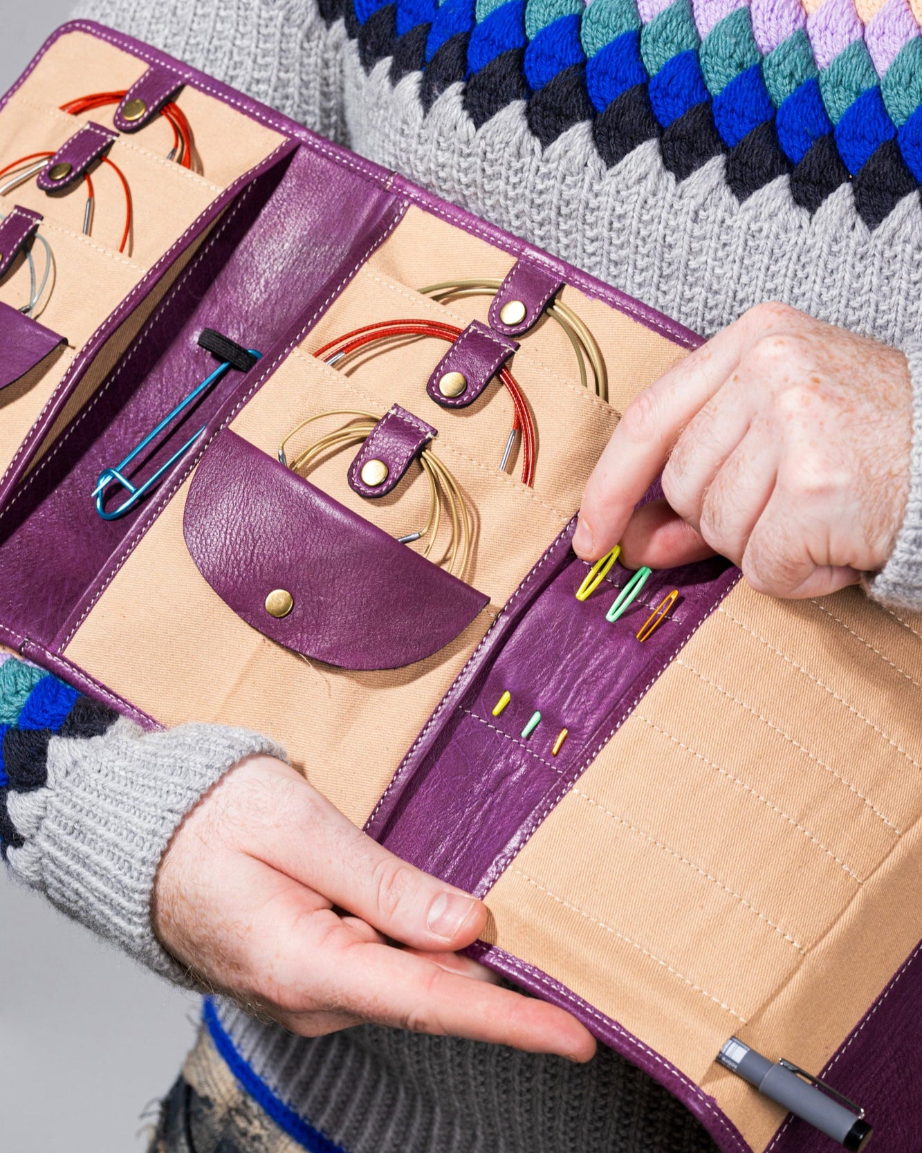 This image shows the inside of Project 14 - Aubergine, filled with needles and other knitting accessories. The bag is part of the collaboration between Re:Designed and Westknits. Stephen West is holding the bag. 