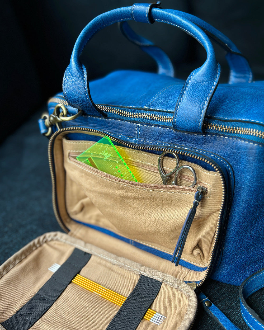 This image shows a denim project bag from the Westknits x Re:Designed collaboration filled with needles and notions in its front pocket. 