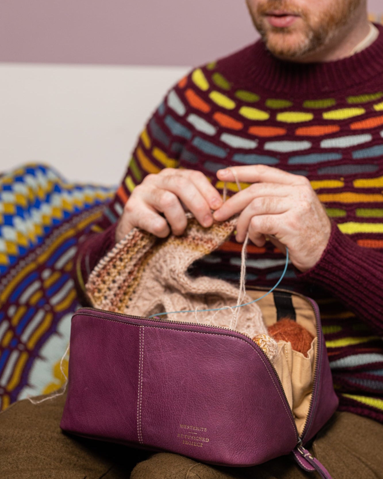 This image shows Stephen West knitting a project while his yarn is stored in an aubergine project bag, part of the collaboration between Westknits and Re:Designed. 
