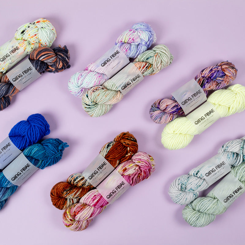 This image shows various skeins of Qing Fibre Merino Chunky on various colours on a lilac background. 